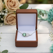 Necklace with a green gemstone in a wooden box surrounded by flowers on a white surface