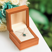 Open wooden jewelry box with a necklace featuring a green gemstone, surrounded by flowers.