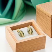 Pair of earrings in a wooden box with a green fabric background