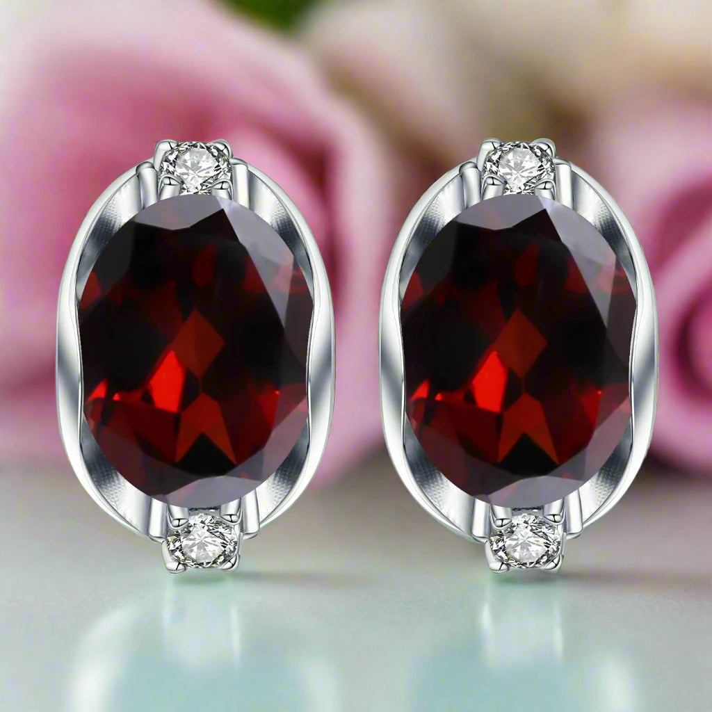 Pair of earrings with red gemstones and silver settings on a white background