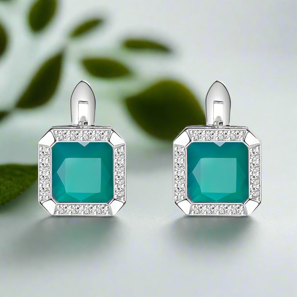 Pair of earrings with teal gemstones and silver frames on a white background