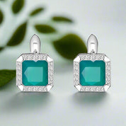 Pair of earrings with teal gemstones and silver frames on a white background