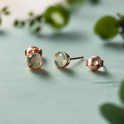 Pair of rose gold earrings with green gemstones on a dark surface