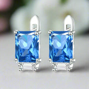 Pair of silver earrings with blue gemstones on a white background