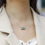 Necklace with a green gemstone pendant worn by a person in a beige coat.
