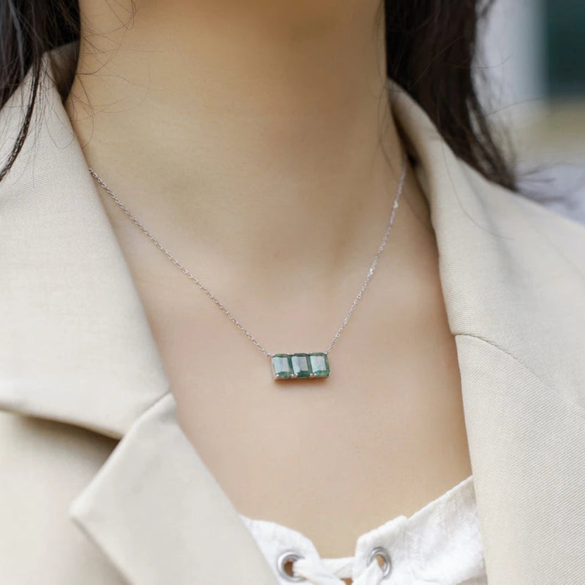 Necklace with a green gemstone pendant worn by a person in a beige coat.