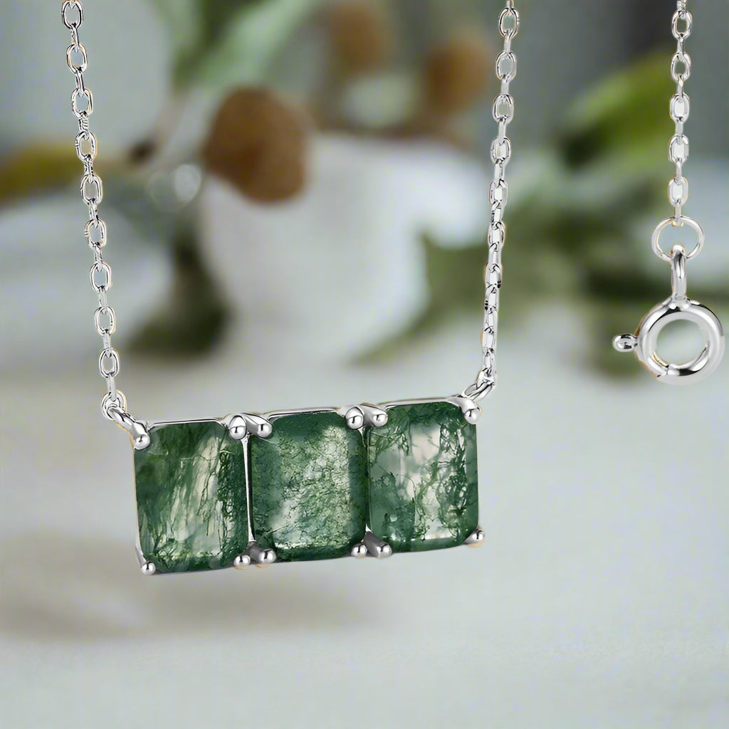 Silver necklace with green gemstones against a blurred natural background