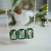 Silver necklace with green gemstones against a blurred natural background