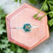 Ring with a blue gemstone on a pink hexagonal cushion with flowers in the background