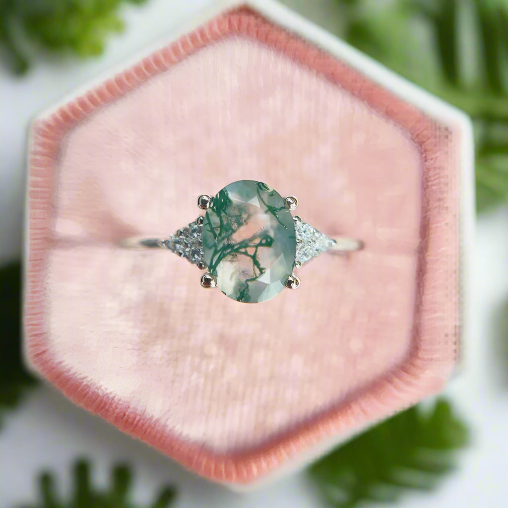 Ring with a green gemstone and diamond accents on a pink fabric background