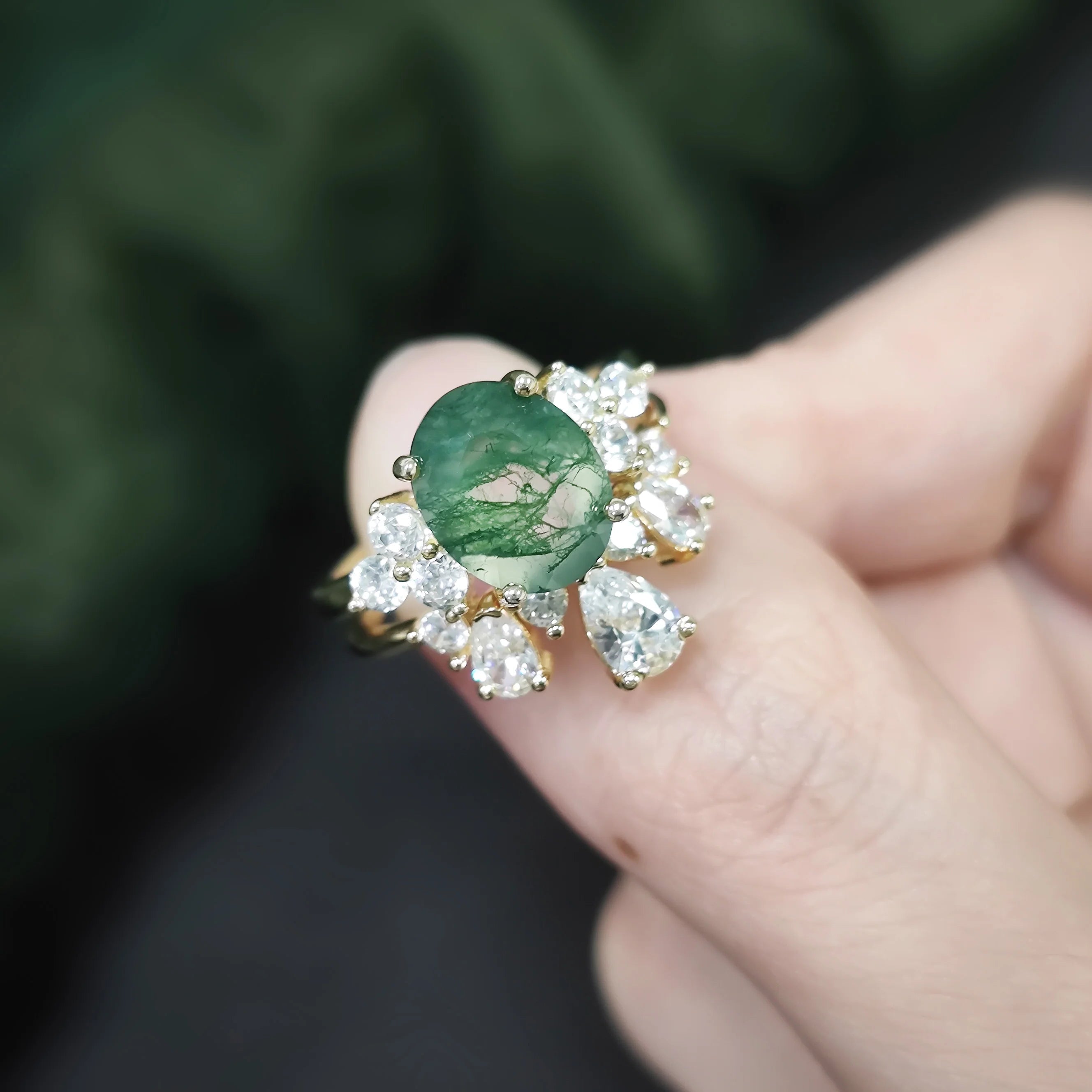 Ring with a green gemstone and diamonds on a finger against a blurred green background