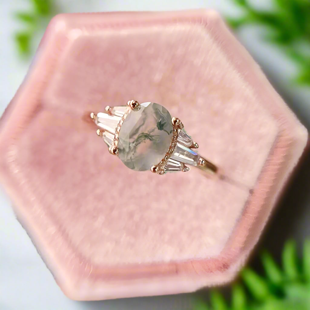 Ring with a green gemstone and rose gold accents on a pink velvet cushion