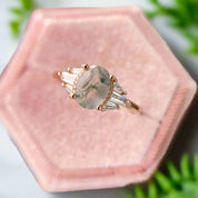 Ring with a green gemstone and rose gold accents on a pink velvet cushion