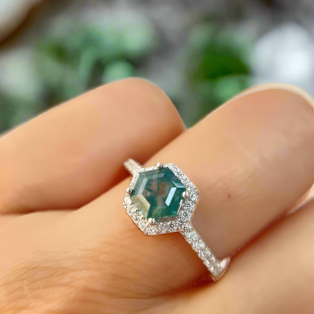 Ring with a green gemstone on a finger against a blurred background