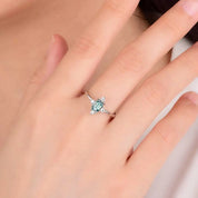 Ring with a green gemstone on a hand against a neutral background