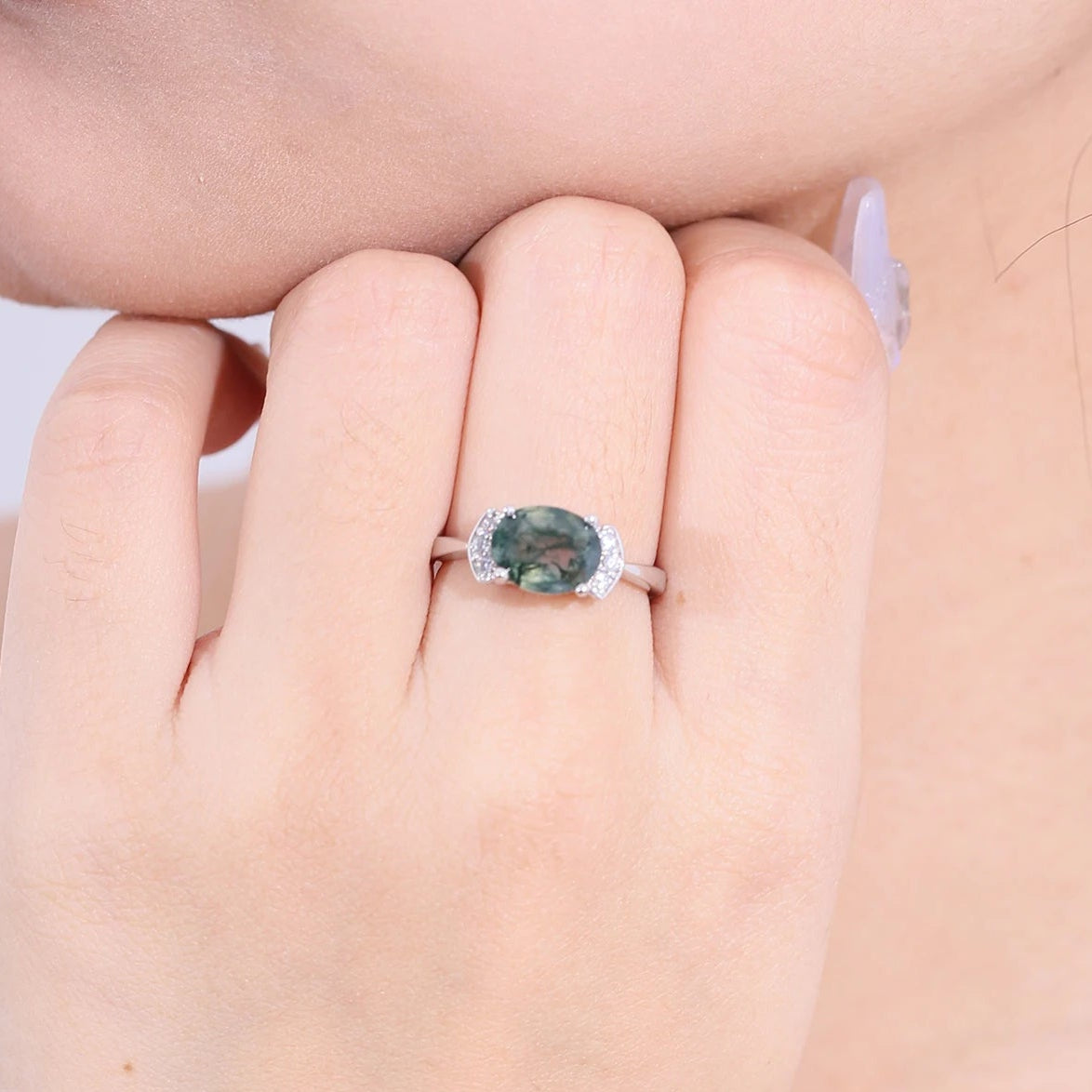 Ring with a green gemstone on a hand against a neutral background