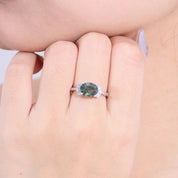 Ring with a green gemstone on a hand against a neutral background