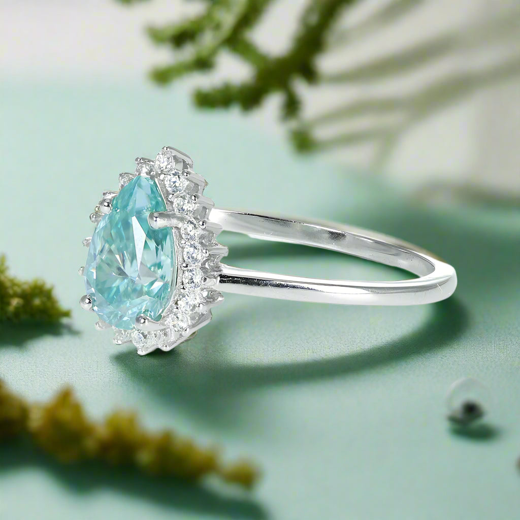 Ring with a pear-shaped blue gemstone and diamond accents on a white background