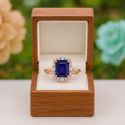 Ring with a purple gemstone in a wooden box against a blurred floral background