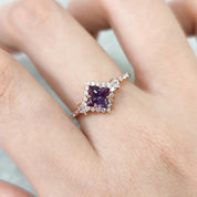 Ring with a purple gemstone on a finger against a neutral background