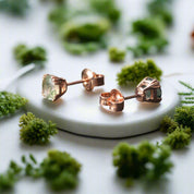 Rose gold earrings with green gemstones on a dark surface