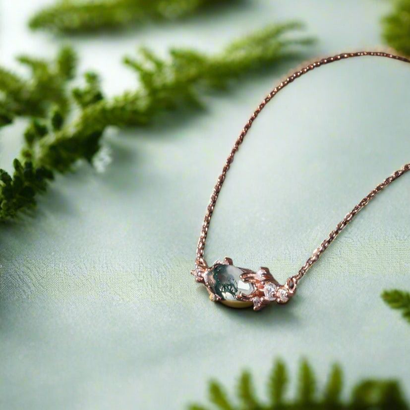 Rose gold necklace with a green gemstone on a dark surface