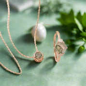 Rose gold necklace with green gemstones on a beige surface