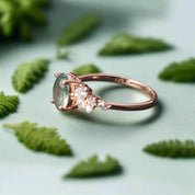 Rose gold ring with a green gemstone and diamonds on a dark surface
