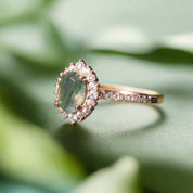 Rose gold ring with a green gemstone and diamonds on a dark surface