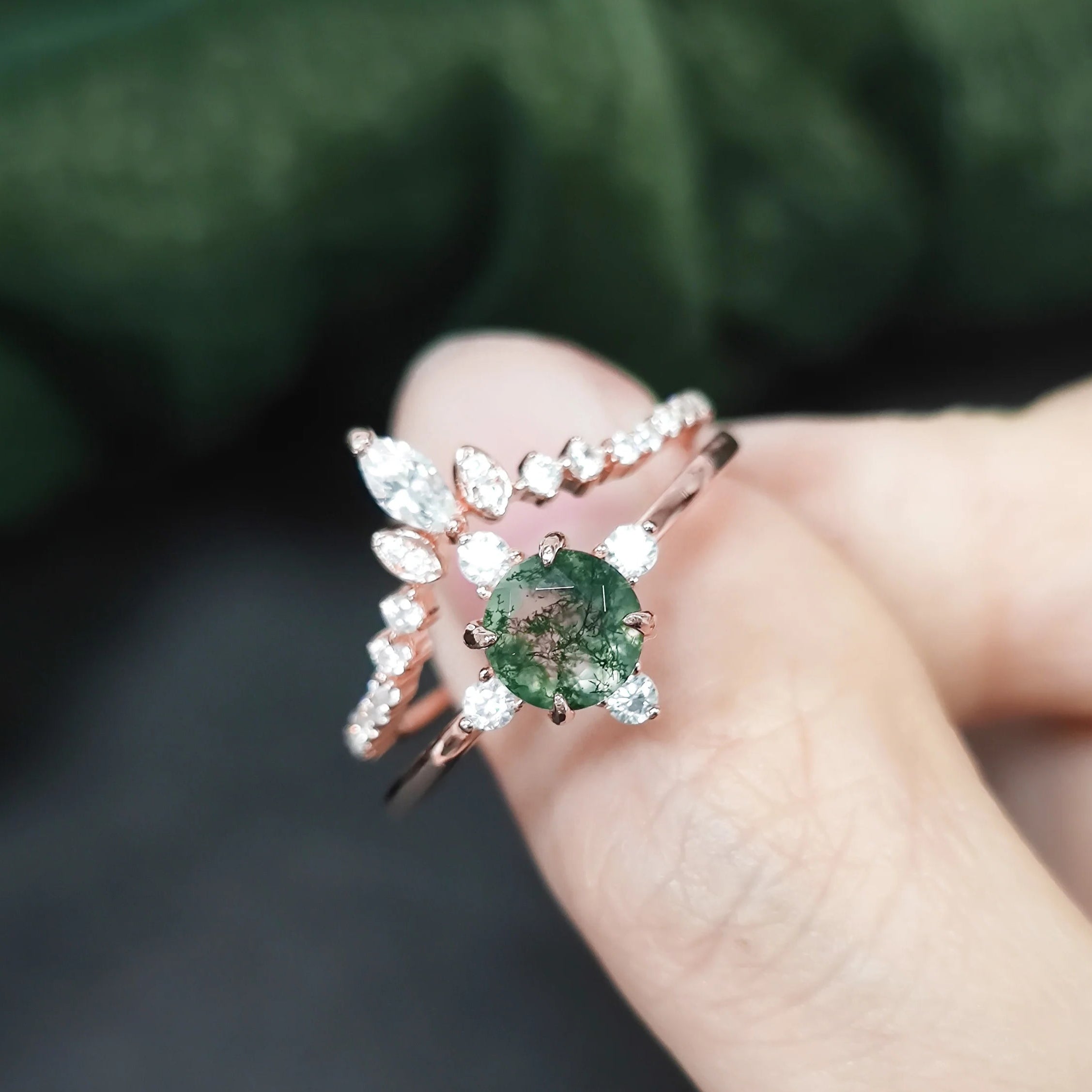 Rose gold ring with a green gemstone held in a hand against a blurred green background