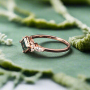 Rose gold ring with a green gemstone on a dark surface