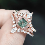 Rose gold ring with green gemstone held in a hand against a blurred background