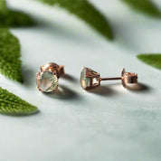 Rose gold stud earrings with green gemstones on a dark surface