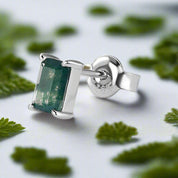 Silver earring with green gemstone on a light gray background