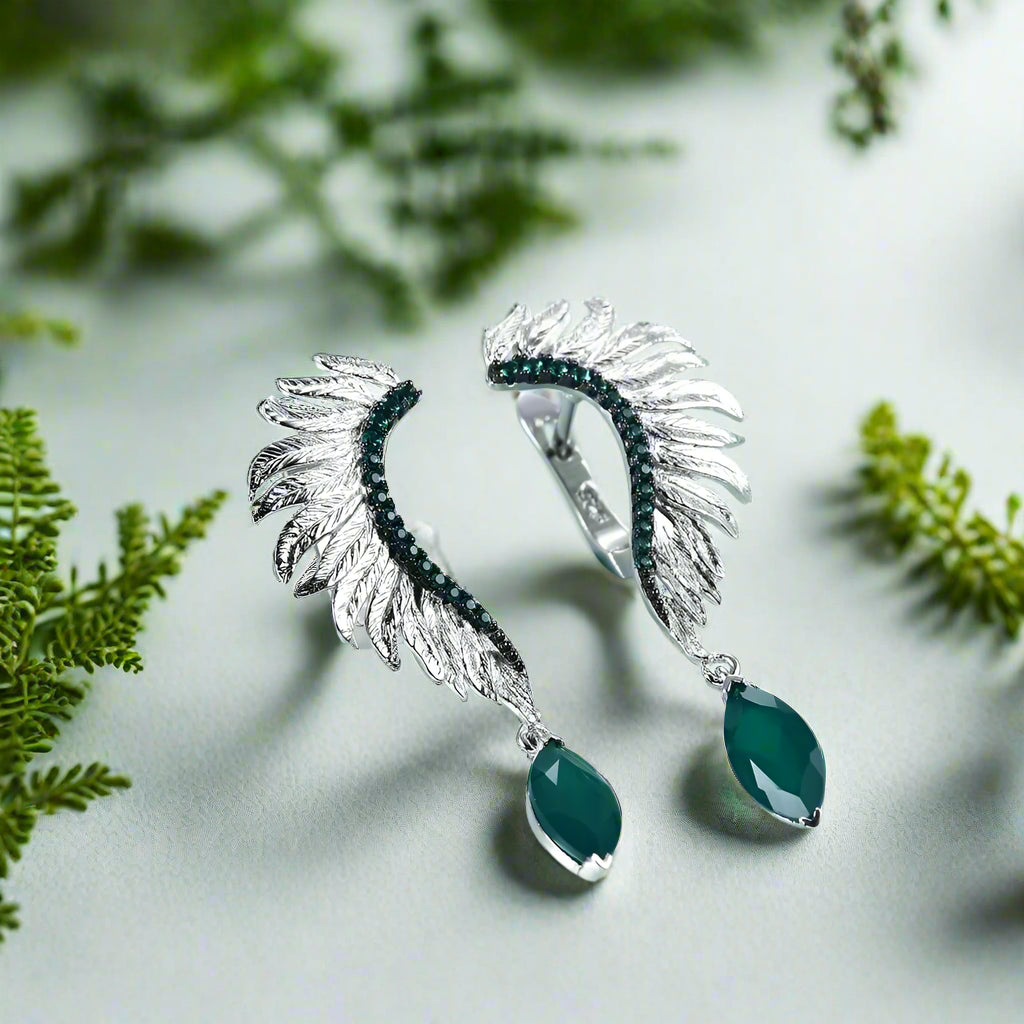 Silver earrings with green stones on a light blue background