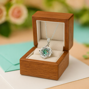 Silver necklace with a green pendant in an open wooden jewelry box on a light surface.