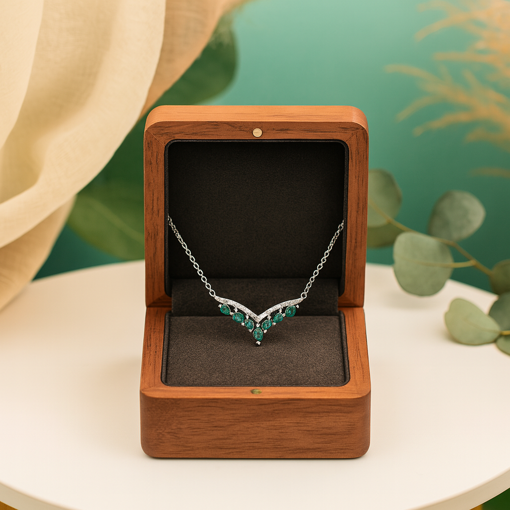 Silver necklace with green gemstones in a wooden box on a white surface with greenery in the background