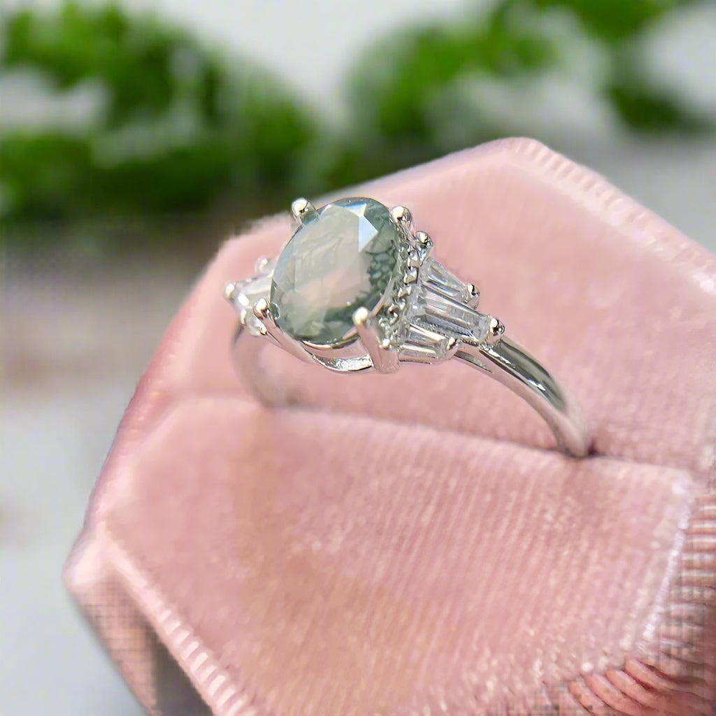 Silver ring with a green gemstone held on a pink cushion