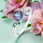 Silver ring with a large purple gemstone and smaller green and clear stones on a white background