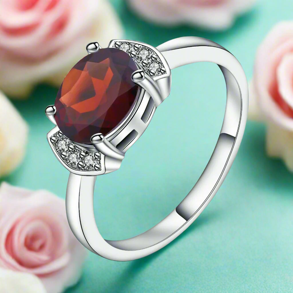 Silver ring with a red gemstone and small diamonds on a white background