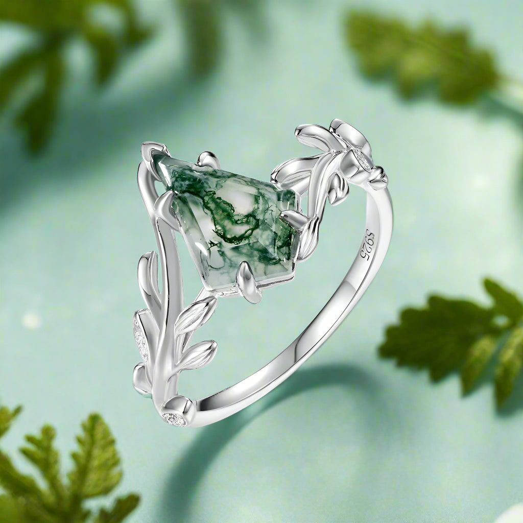 Silver ring with green gemstone and leaf design on a white background