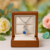 Silver swan necklace with blue gem in a wooden box with flowers in the background
