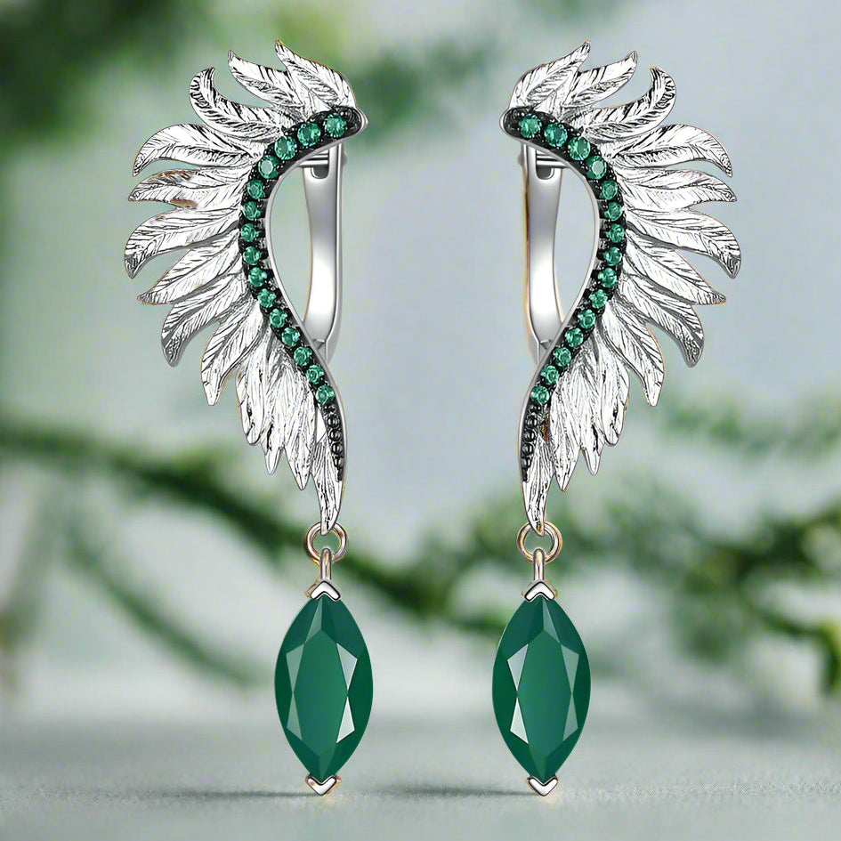 Silver wing-shaped earrings with green gemstones on a white background