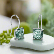 Green gemstone earrings with silver hooks on a light gray background