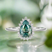 Teardrop-shaped green gemstone ring with diamond accents on a white background
