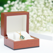 Wooden jewelry box with a green gemstone pendant on a blurred natural background
