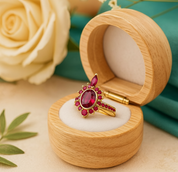 Gold ring with red gemstones in a wooden box on a beige surface with a rose in the background