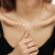 Close-up of a necklace with a pendant and a ring on a person's hand, wearing a black top.