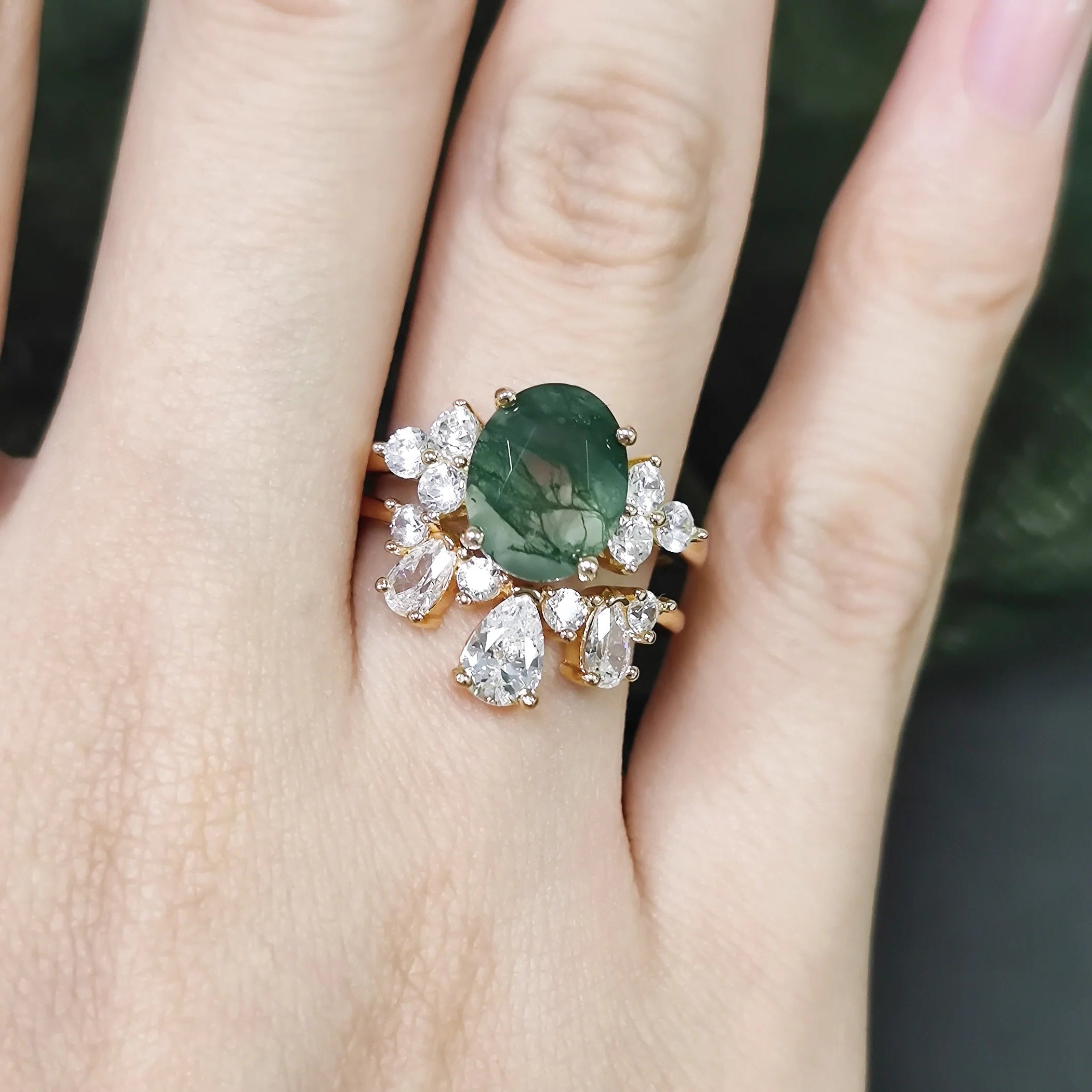 Ring with a green gemstone and diamond accents on a hand against a blurred background