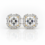 A pair of stud earrings featuring large emerald-cut clear center stones surrounded by baguette and round clear accent stones in a silver-toned setting with small gold accents, shown on a white reflective background.